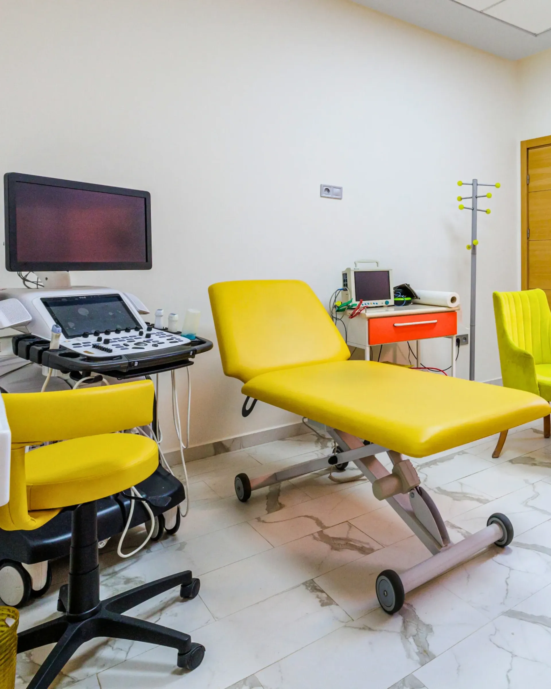 Un cabinet médical avec un lit jaune, des chaises et un appareil à ultrasons.