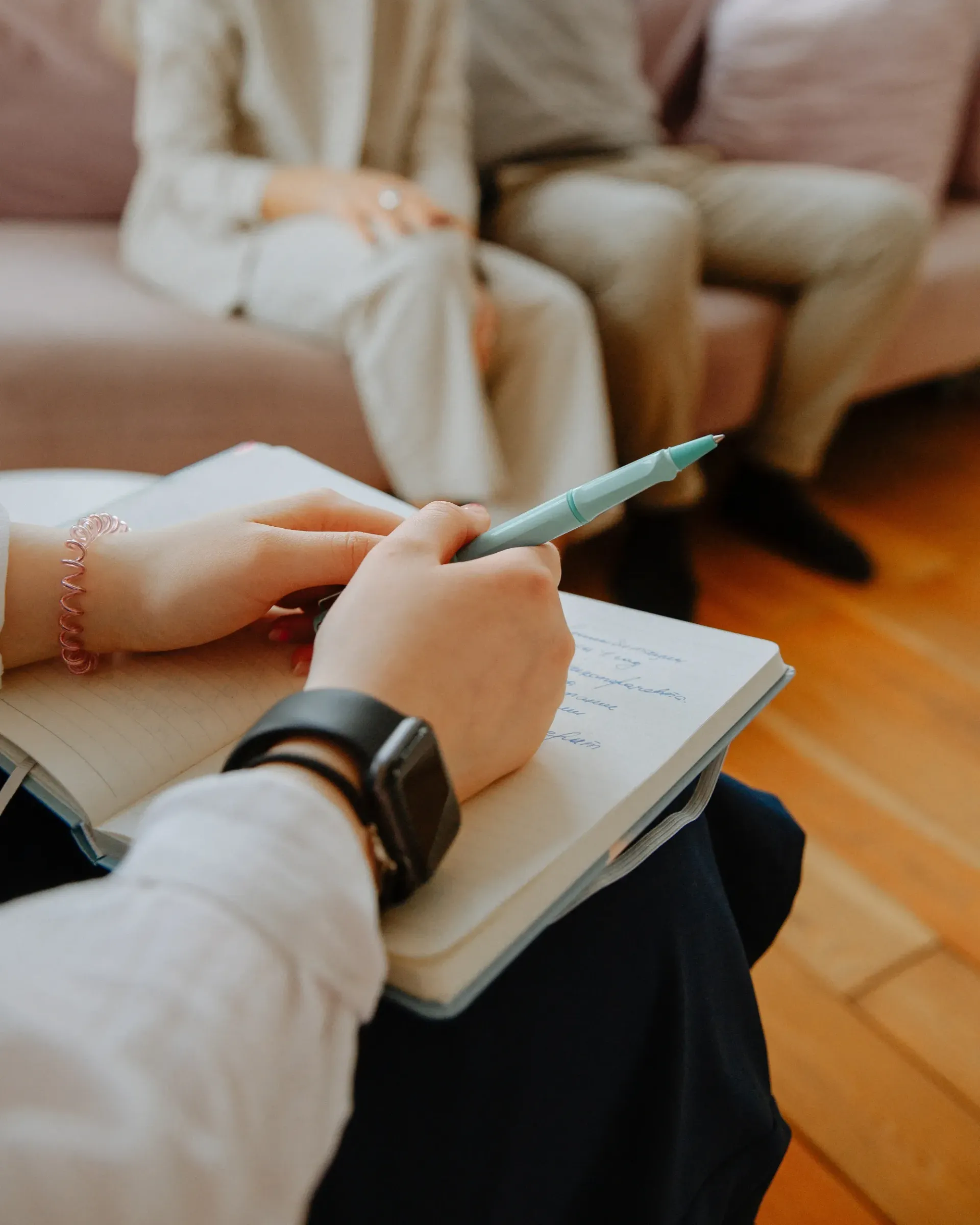 Une personne écrit dans un cahier alors qu'elle est assise sur un canapé.