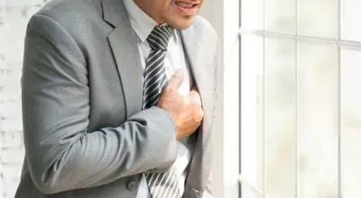 Un homme en costume et cravate se tient la poitrine.