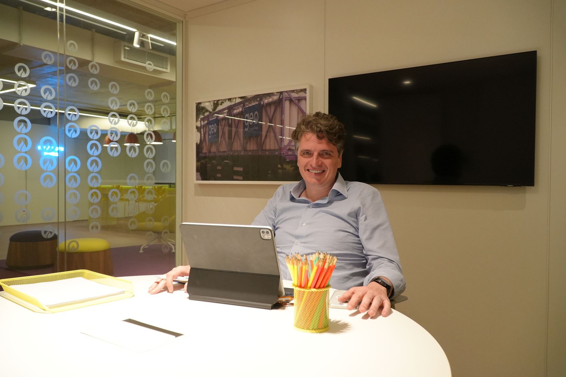 Um homem está sentado à mesa com um laptop e lápis.