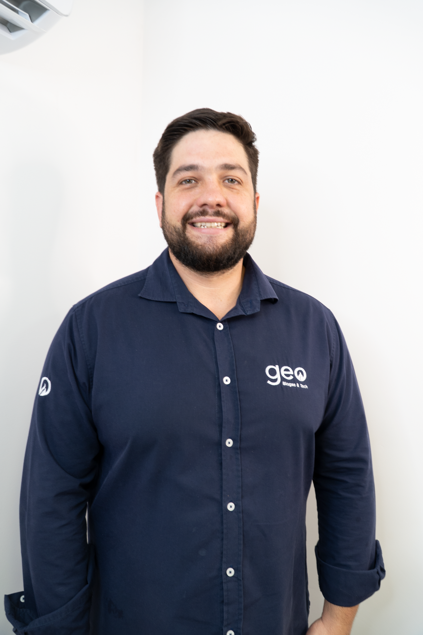 Homem sorrindo para a câmera usando camisa azul escrito Geo