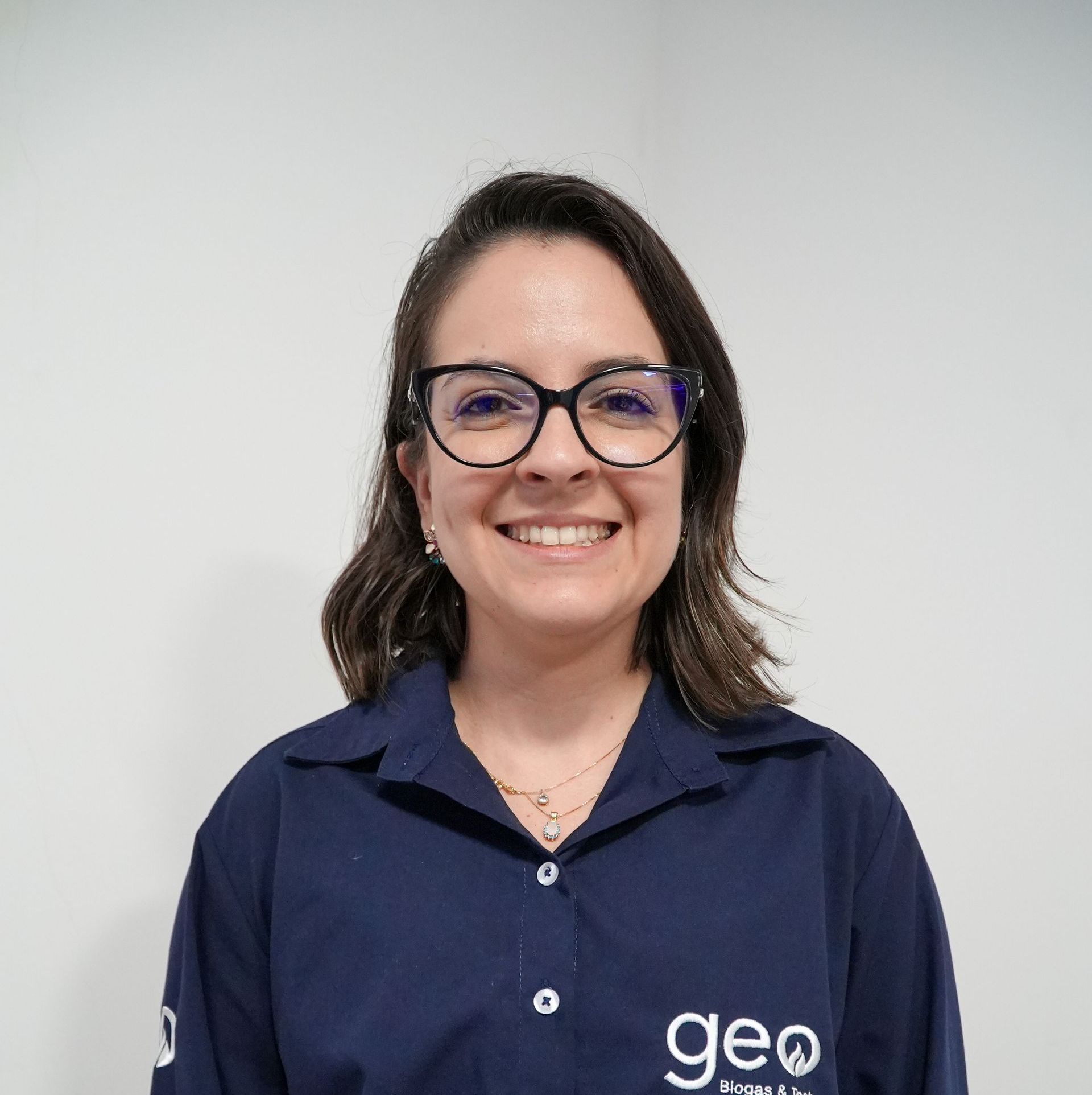 Uma mulher usando óculos e uma camisa azul está sorrindo para a câmera.