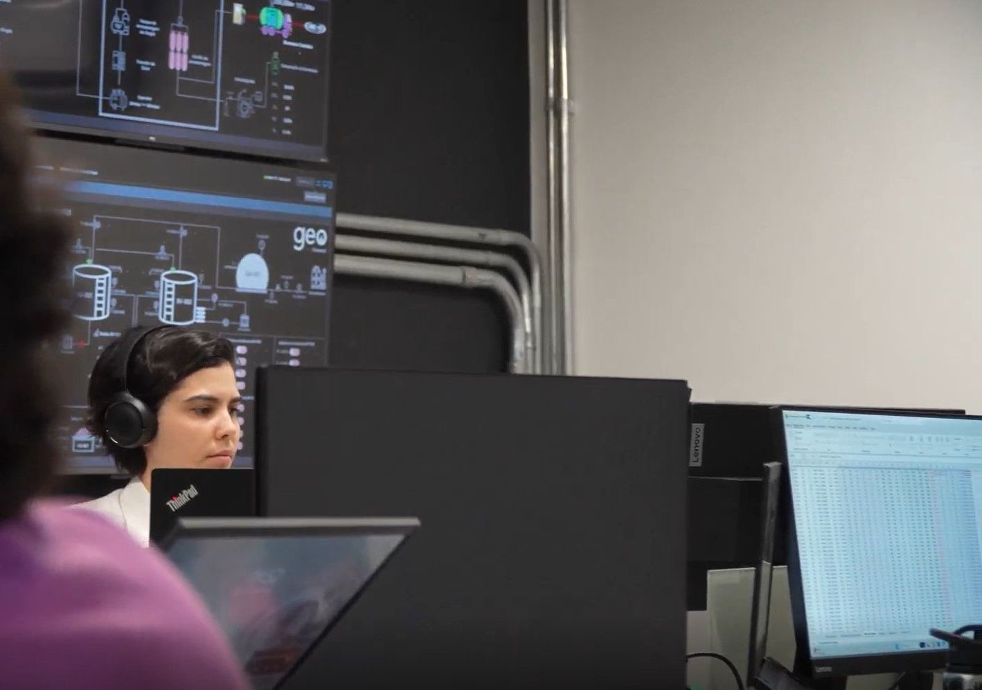 Uma mulher usando fones de ouvido está sentada em frente a um monitor de computador.