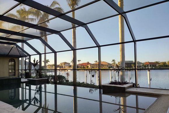 A swimming pool enclosed by a screen patio, overlooking a canal and houses at sunset.