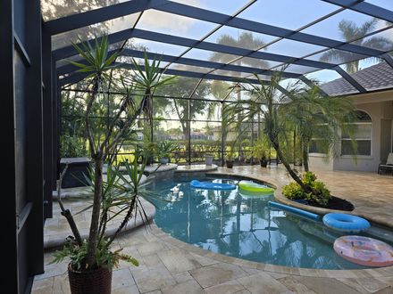A screened-in patio features a kidney-shaped swimming pool with colorful floating tubes, surrounded by stone pavers.