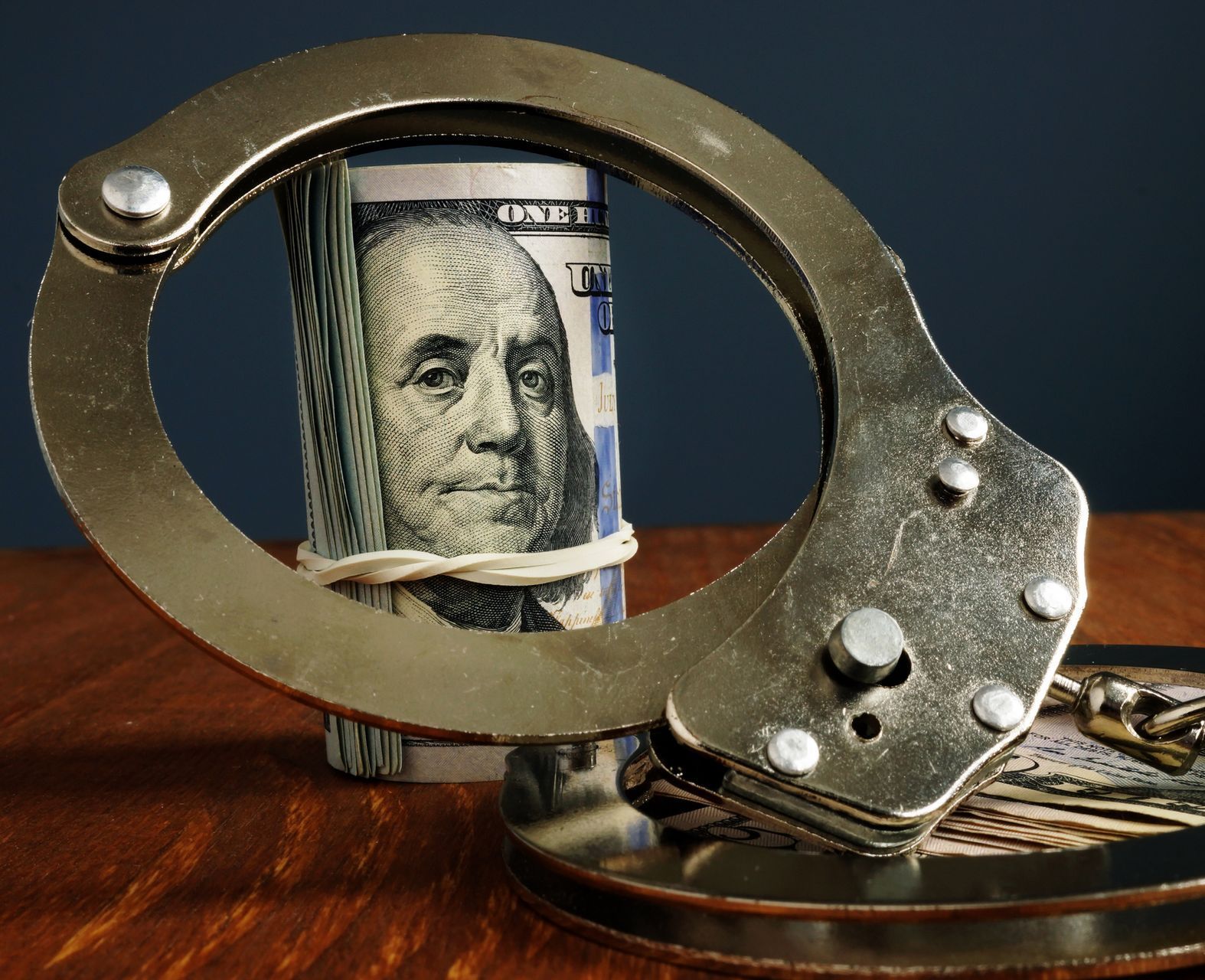 A pair of handcuffs holding a stack of money on a wooden table.