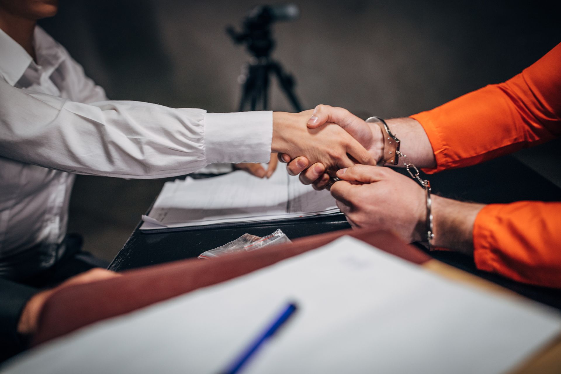 A man in an orange shirt is shaking hands with a man in a white shirt.