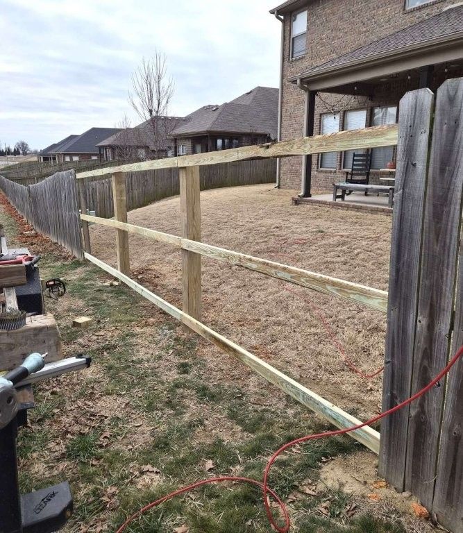 A new wooden fence frame with three horizontal rails stands in a residential backyard next to an existing fence.