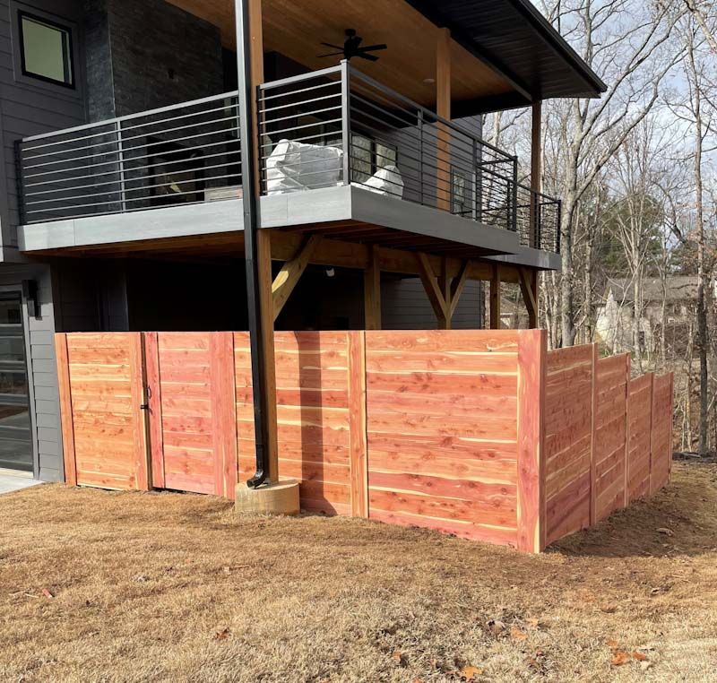 A wooden fence is in front of a house with a balcony.