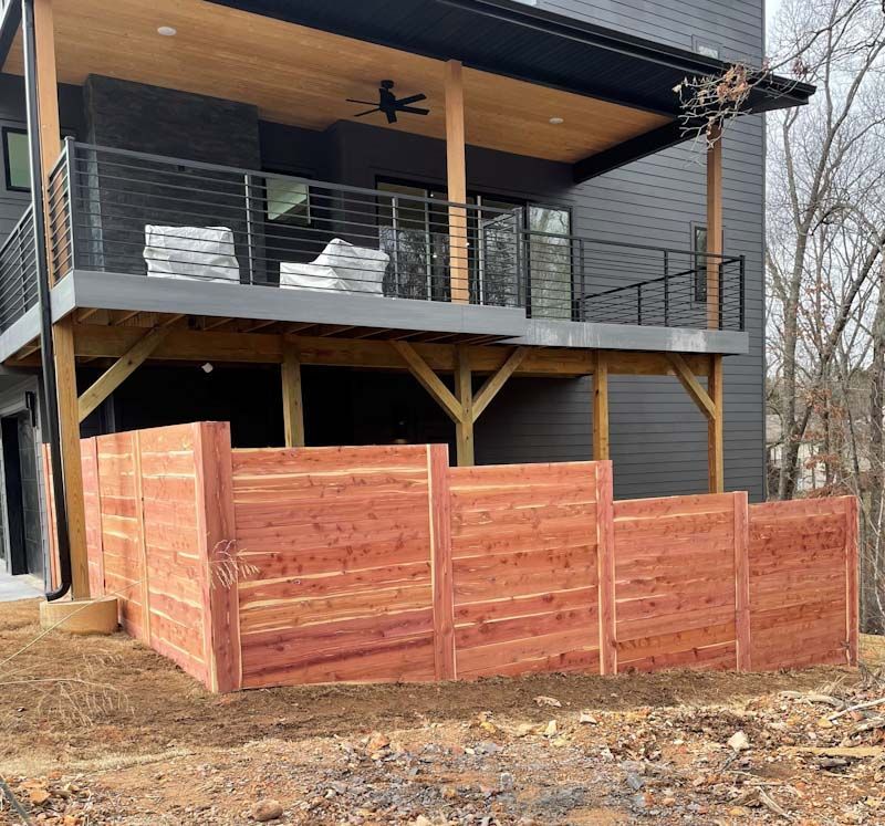 A wooden fence is in front of a house with a balcony.
