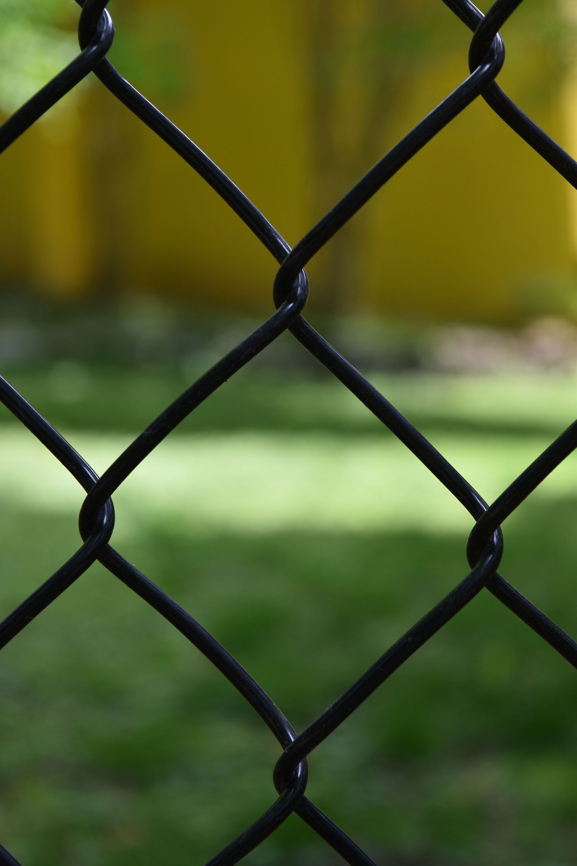 A close up of a chain link fence with a yellow fence in the background