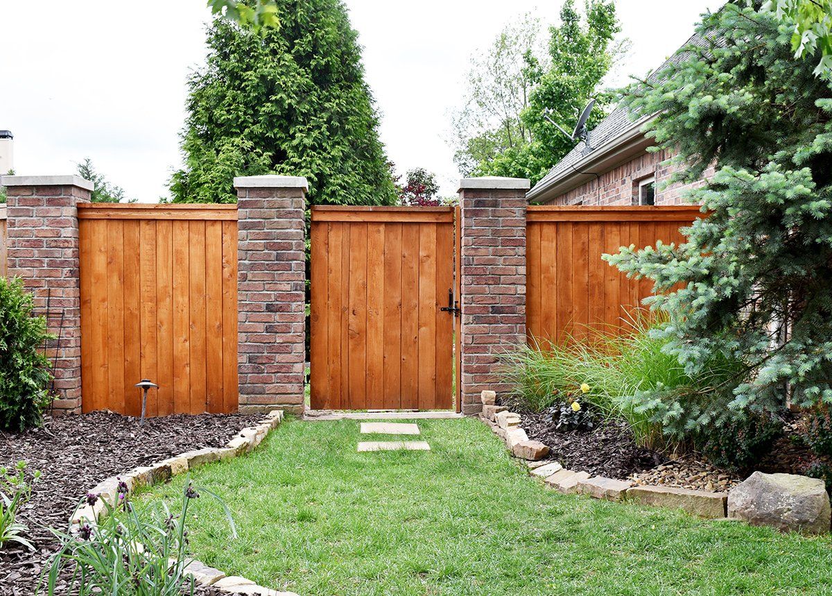 A wooden fence is surrounded by brick pillars in a backyard.