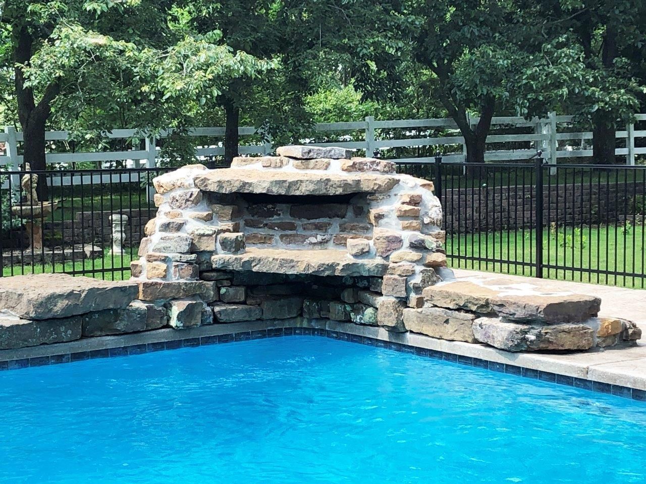a pool with a stone fireplace in the middle of it and a white fence surrounding it