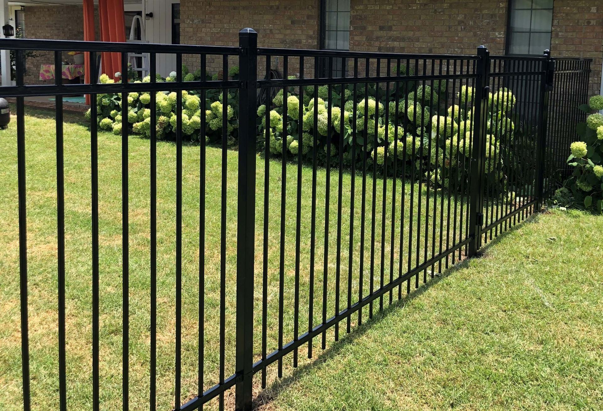 A black metal fence surrounds a lush green lawn in front of a brick house.