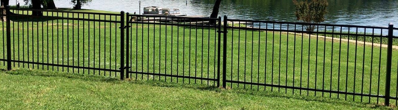 a black metal fence surrounds a lush green lawn next to a lake .