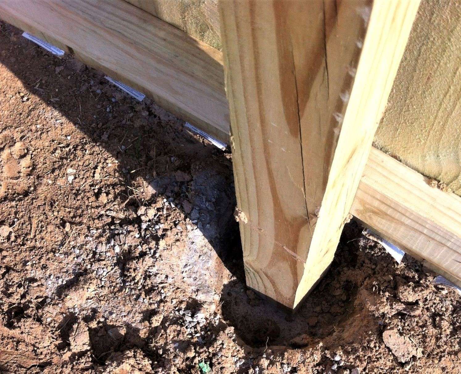 a wooden post in the dirt next to a wooden fence