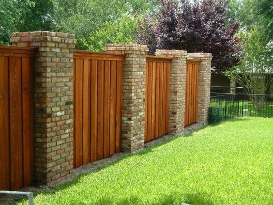 a wooden fence is surrounded by brick pillars in a backyard .