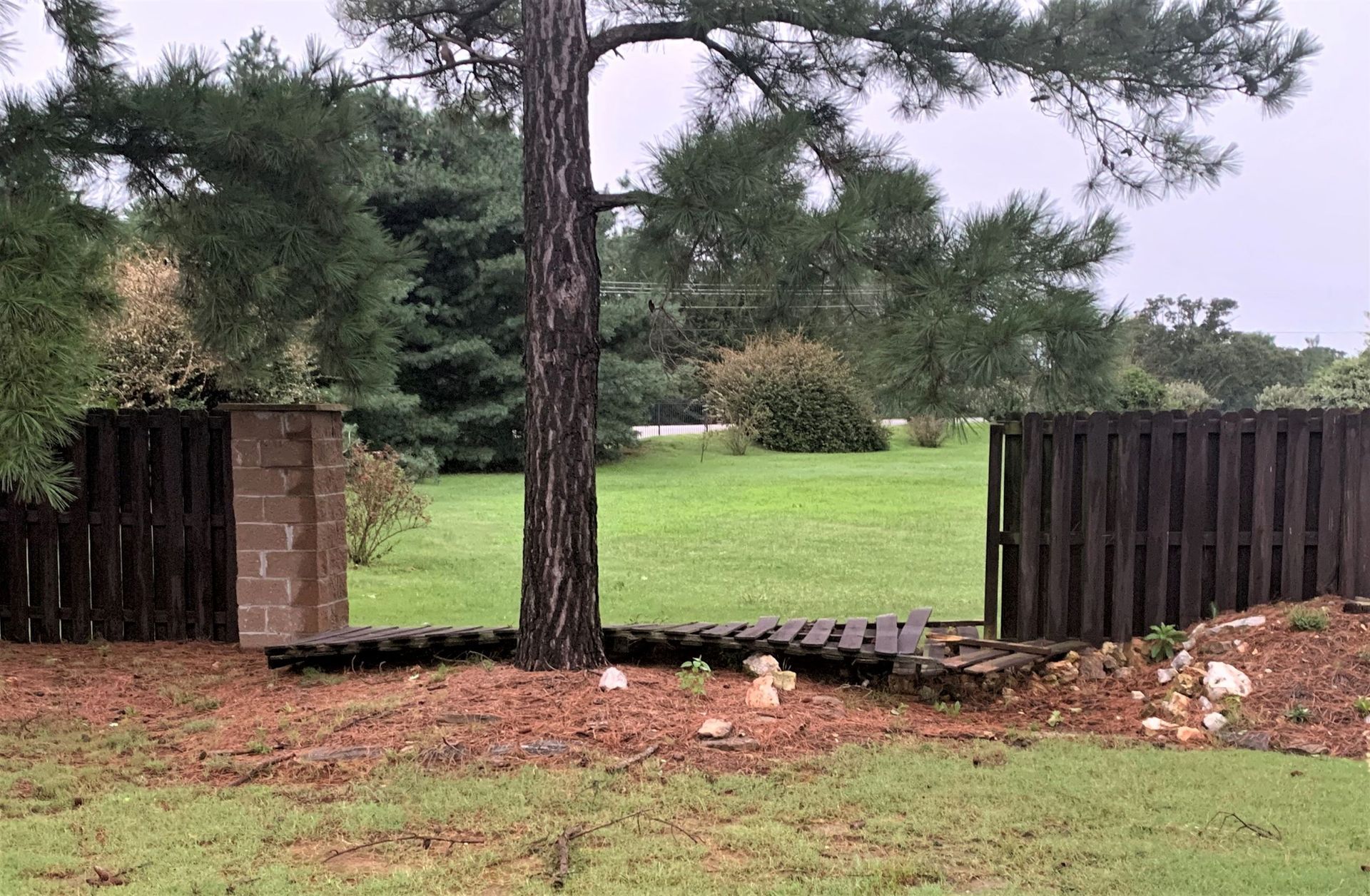a broken wooden fence with a brick pillar in the middle of it