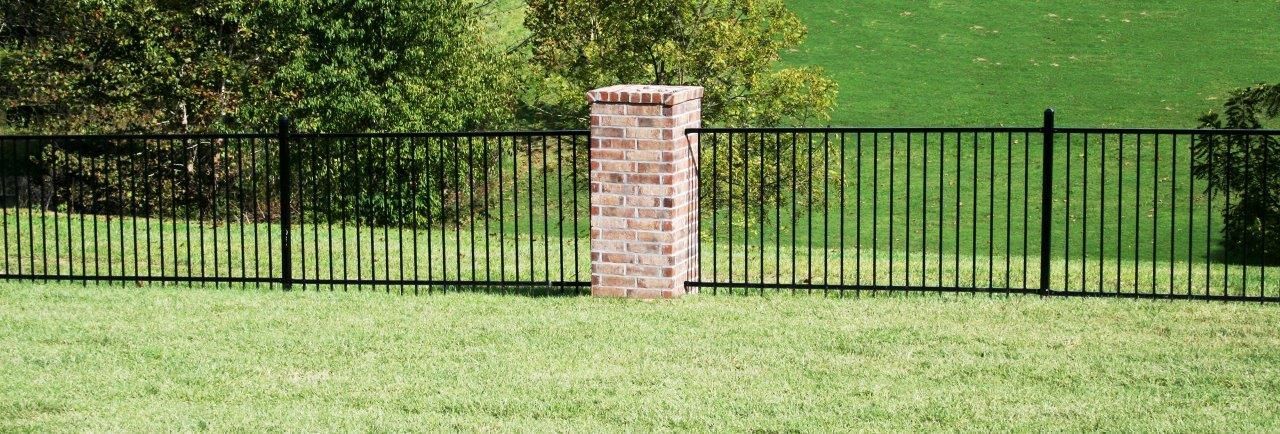 a black metal fence with a brick pillar in the middle of it .