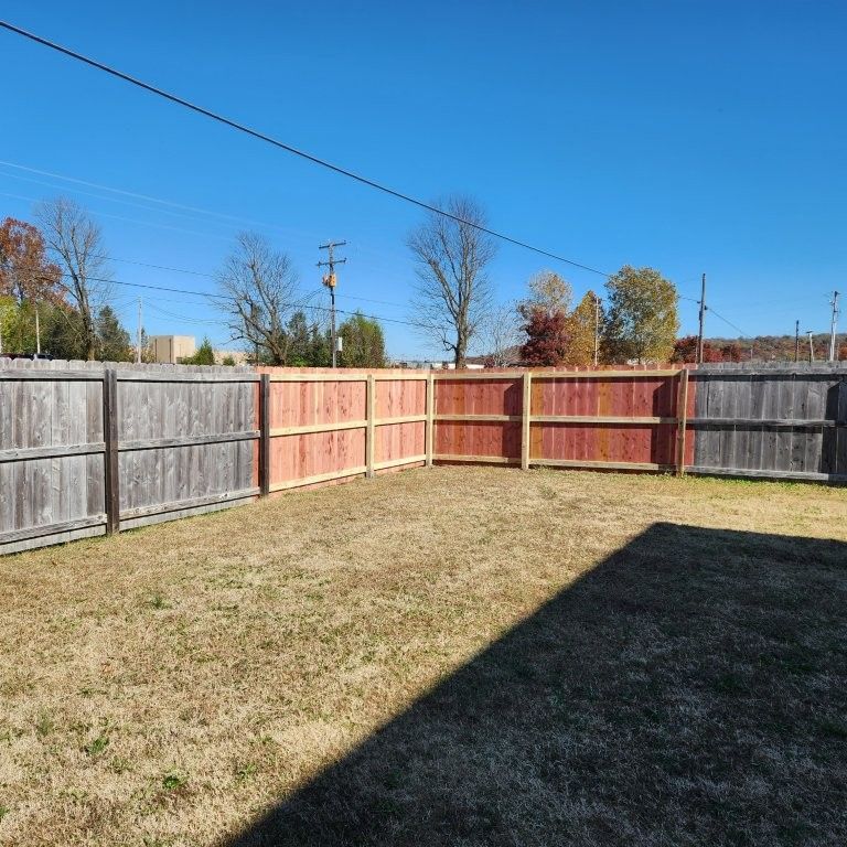 A backyard lawn against a wooden fence that transitions from weathered grey on the ends to fresh, red-stained boards.