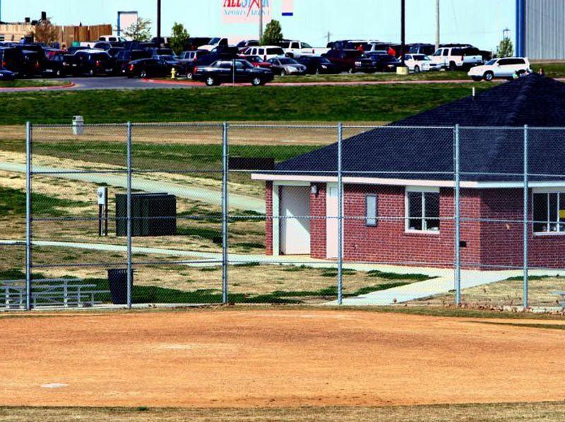 A fence surrounds a baseball field with a brick building in the background