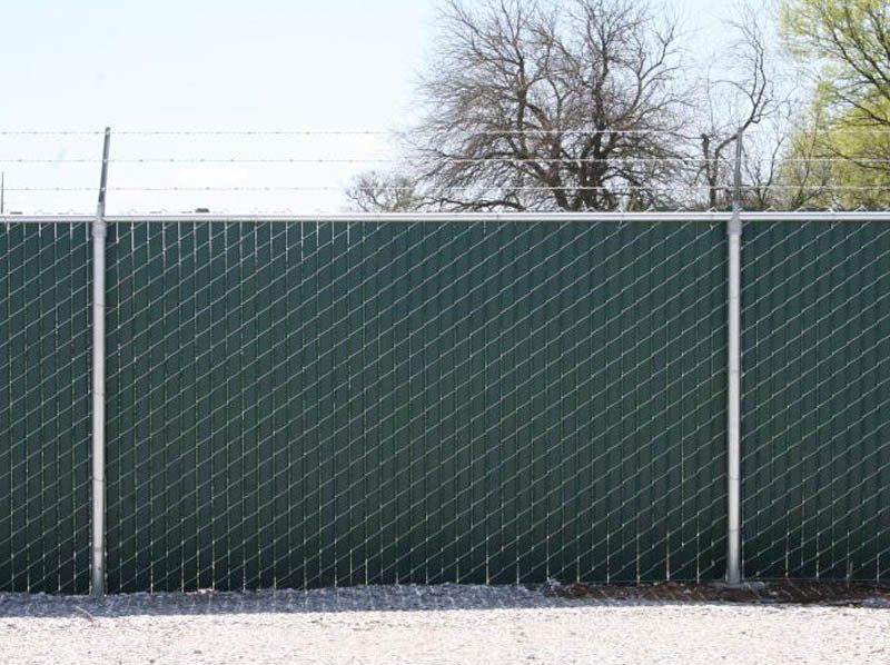 A green chain link fence is surrounded by gravel and trees.