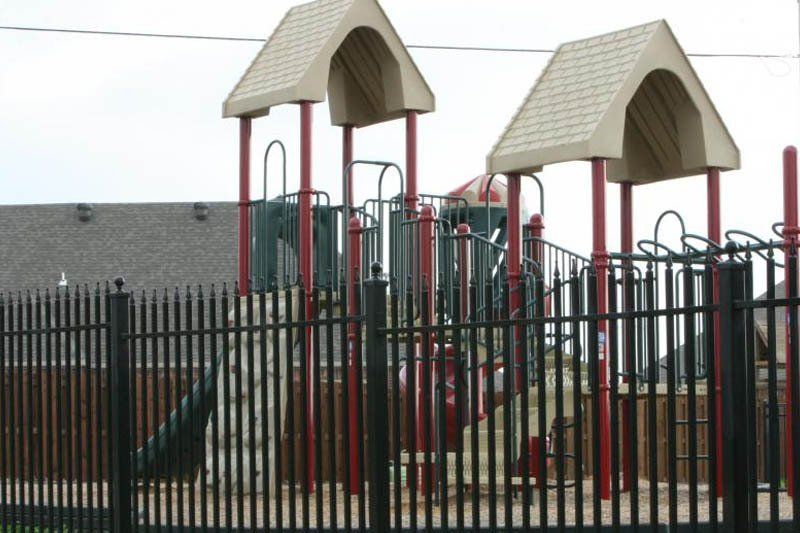 A playground is behind a fence with a house in the background