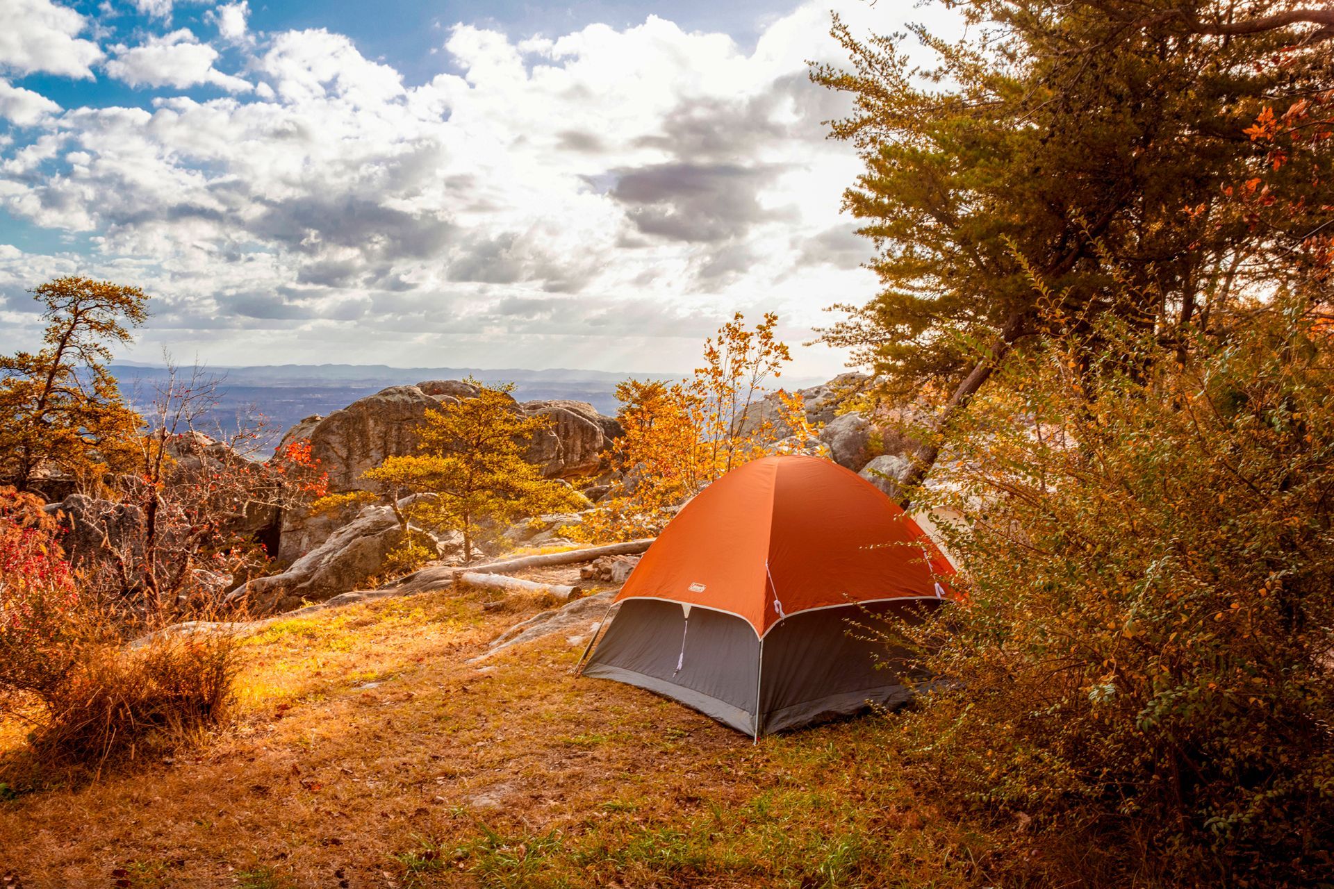 Orange and gray tent on a hilltop, with fall foliage, under a cloudy sky.