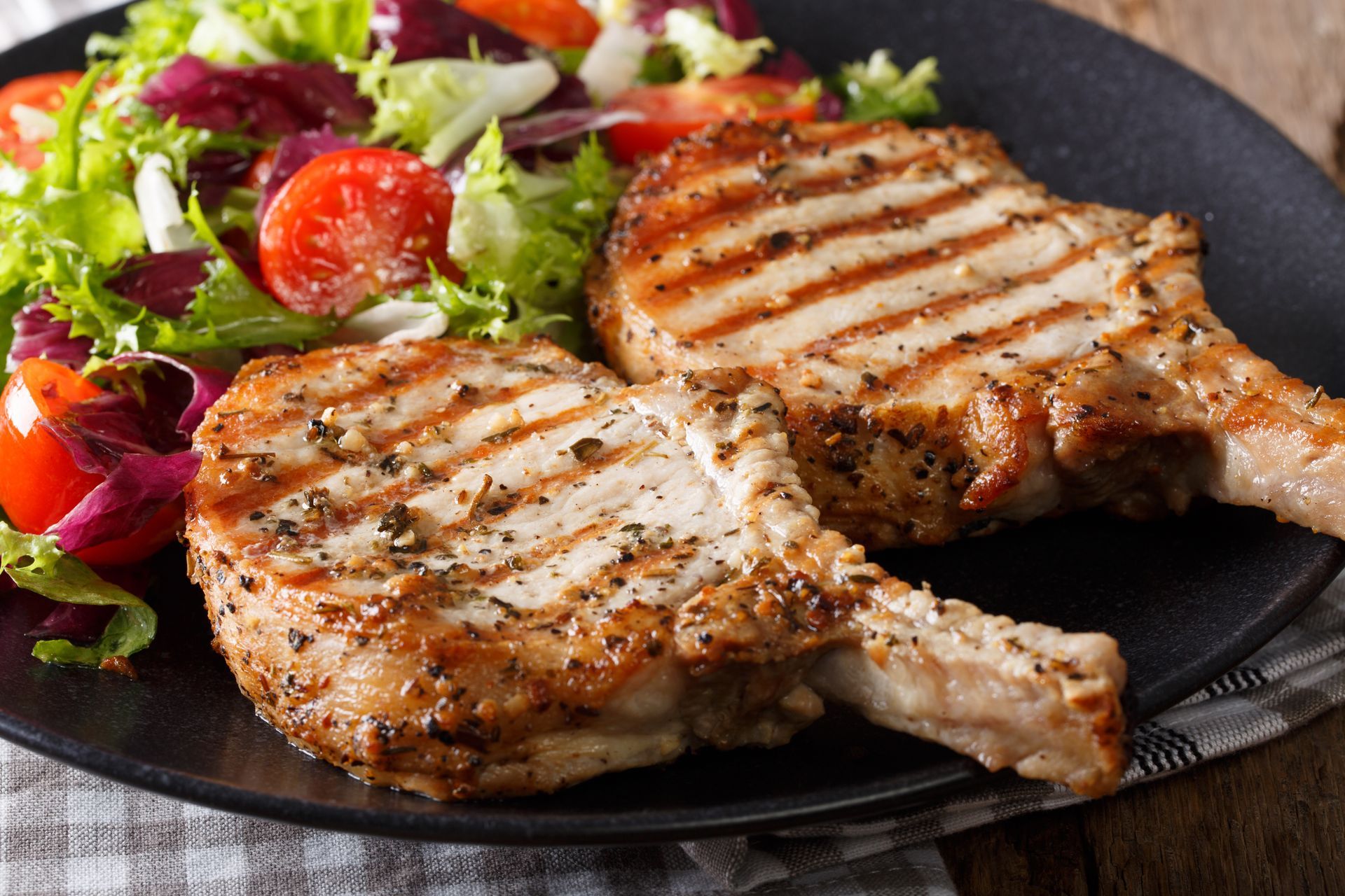 Grilled pork chops with a side salad on a black plate.