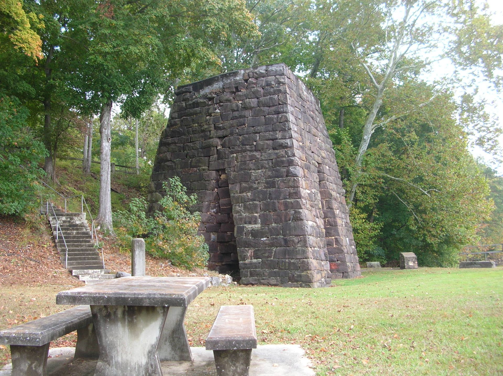 A stone structure resembling a kiln in a grassy park setting, with a picnic table in the foreground.