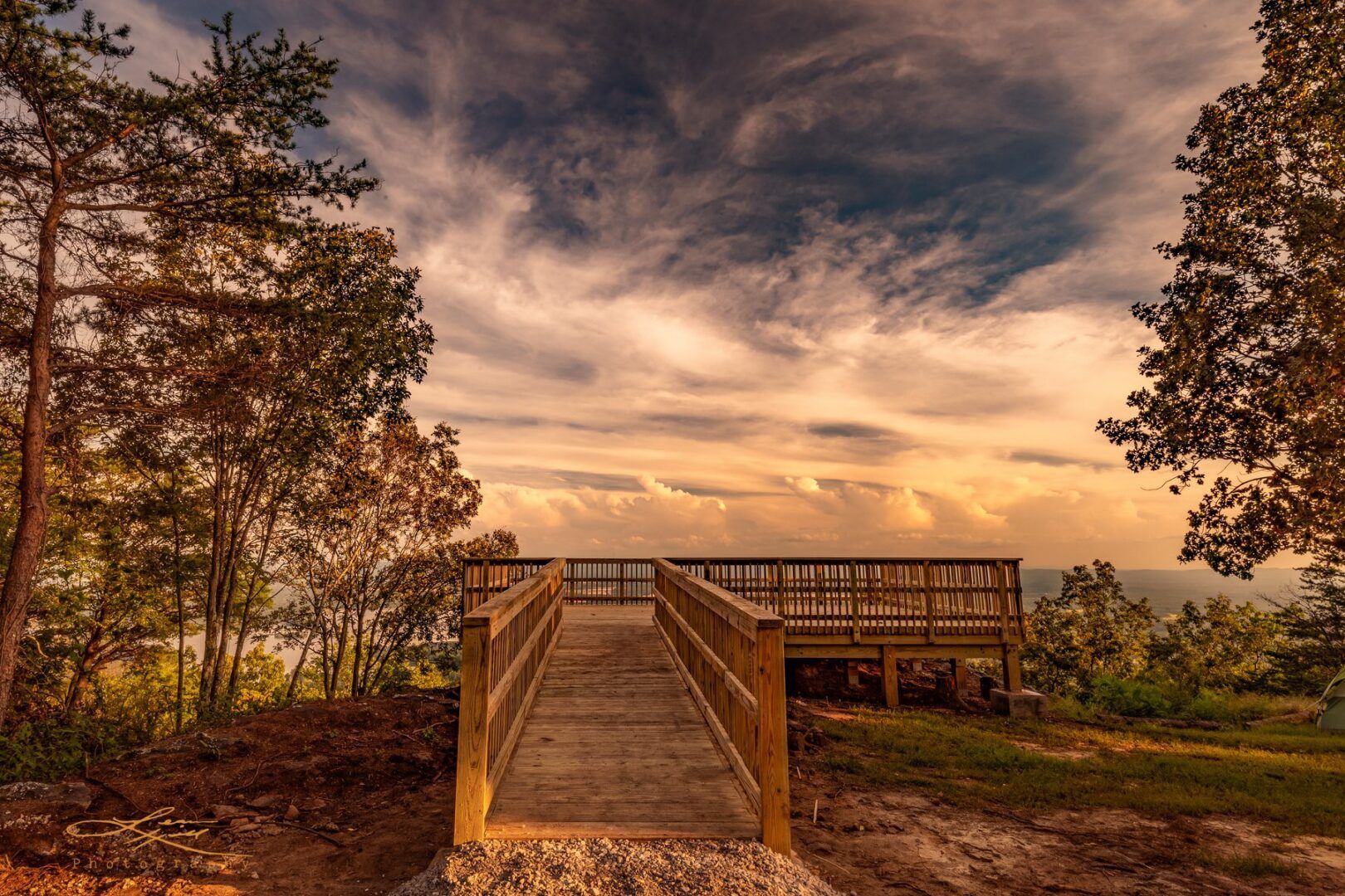 Wooden walkway leads to an overlook with a scenic sunset over the horizon.