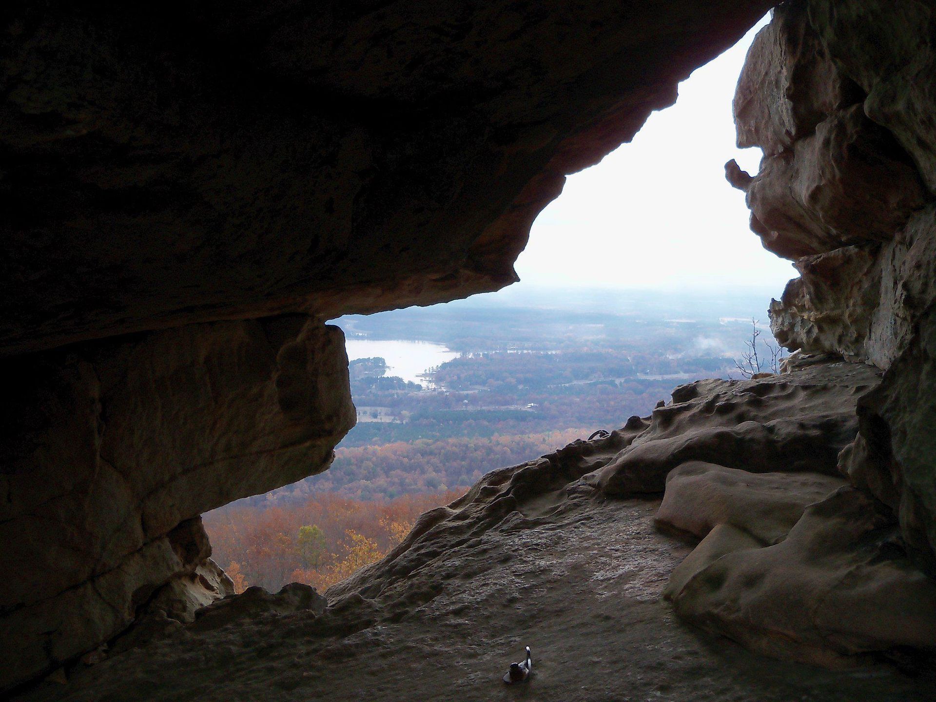 View from a cave opening overlooking a lake and forested landscape.