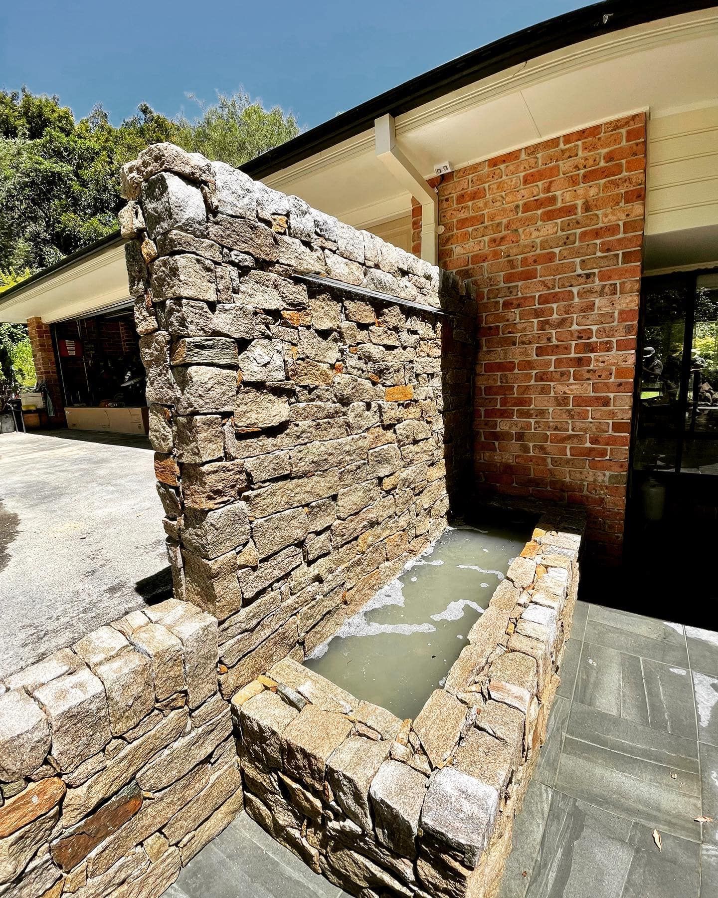 A Stone Water Feature with A Brick House in The Background — Creative Landscapes Coffs Harbour in Moonee Beach, NSW