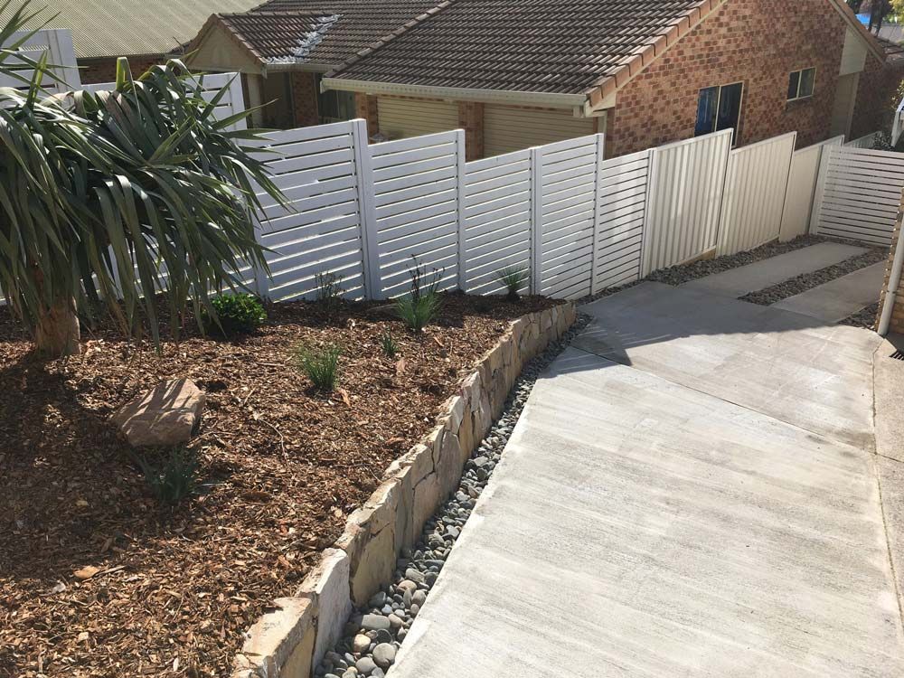 A White Slatted Fence Runs Along a Concrete Driveway — Creative Landscapes Coffs Harbour in Korora, NSW