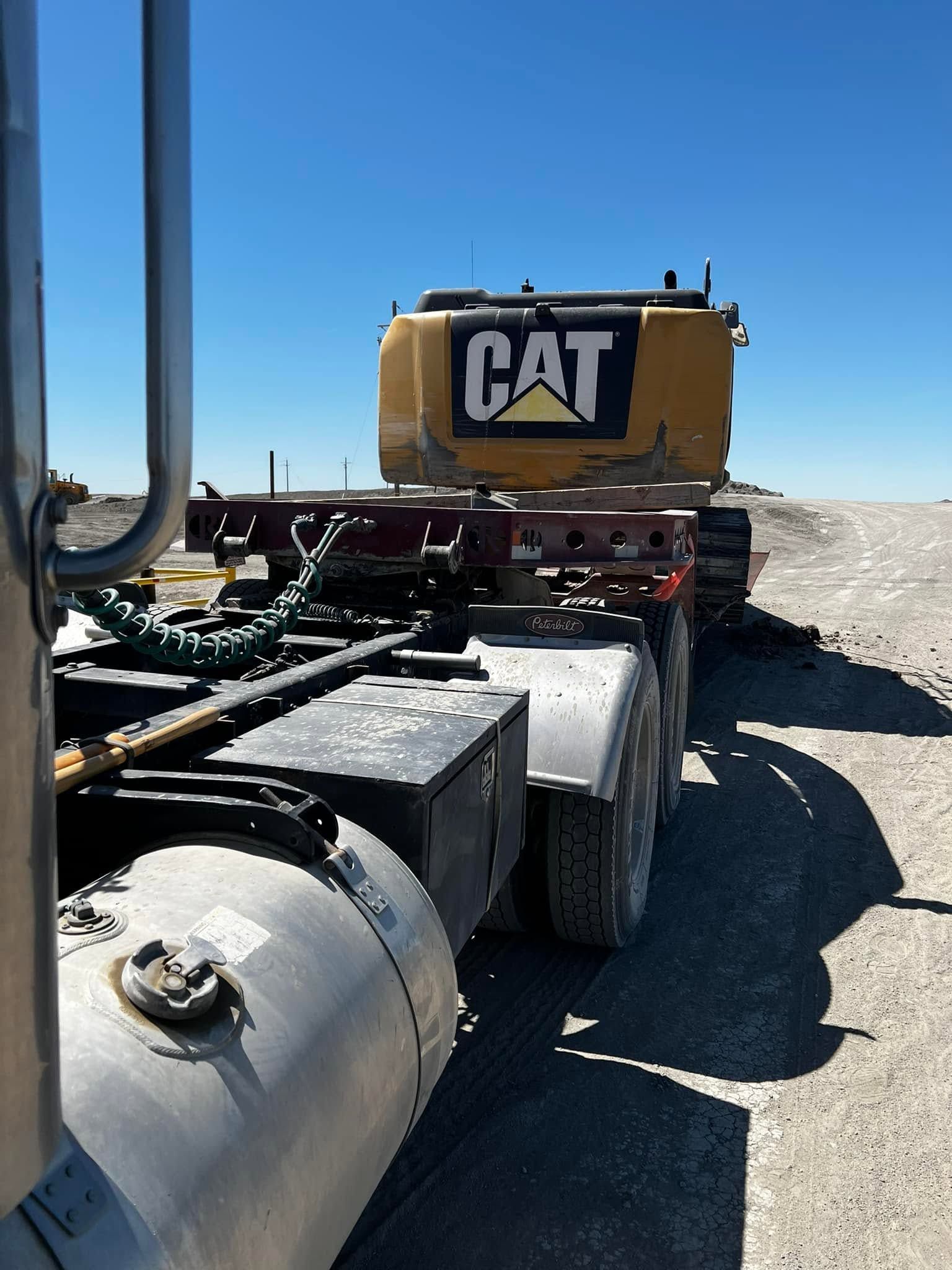 CAT heavy truck parked on a gravel road in a bright desert landscape, viewed from the rear