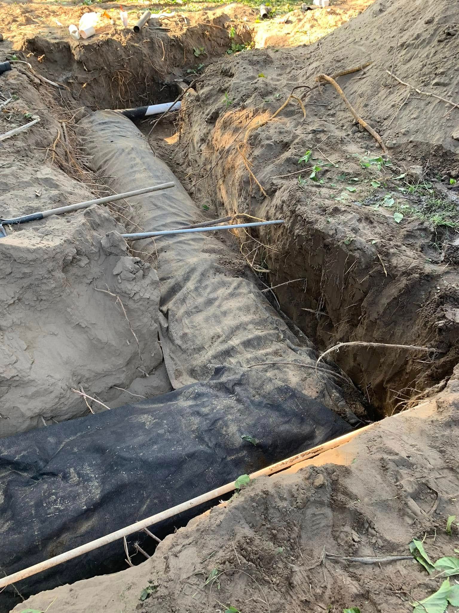 Excavation trench with exposed buried pipe and muddy soil at a construction site
