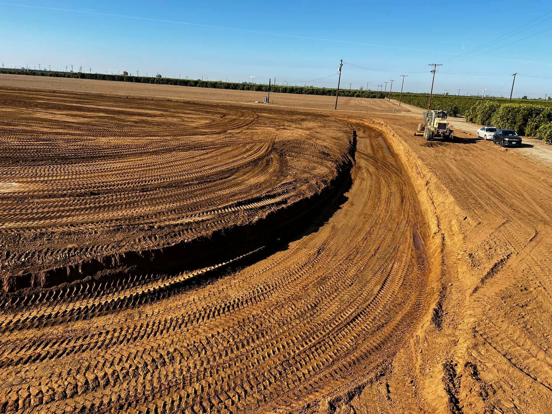 Dirt race track under construction with heavy equipment and tire marks on a sunny day