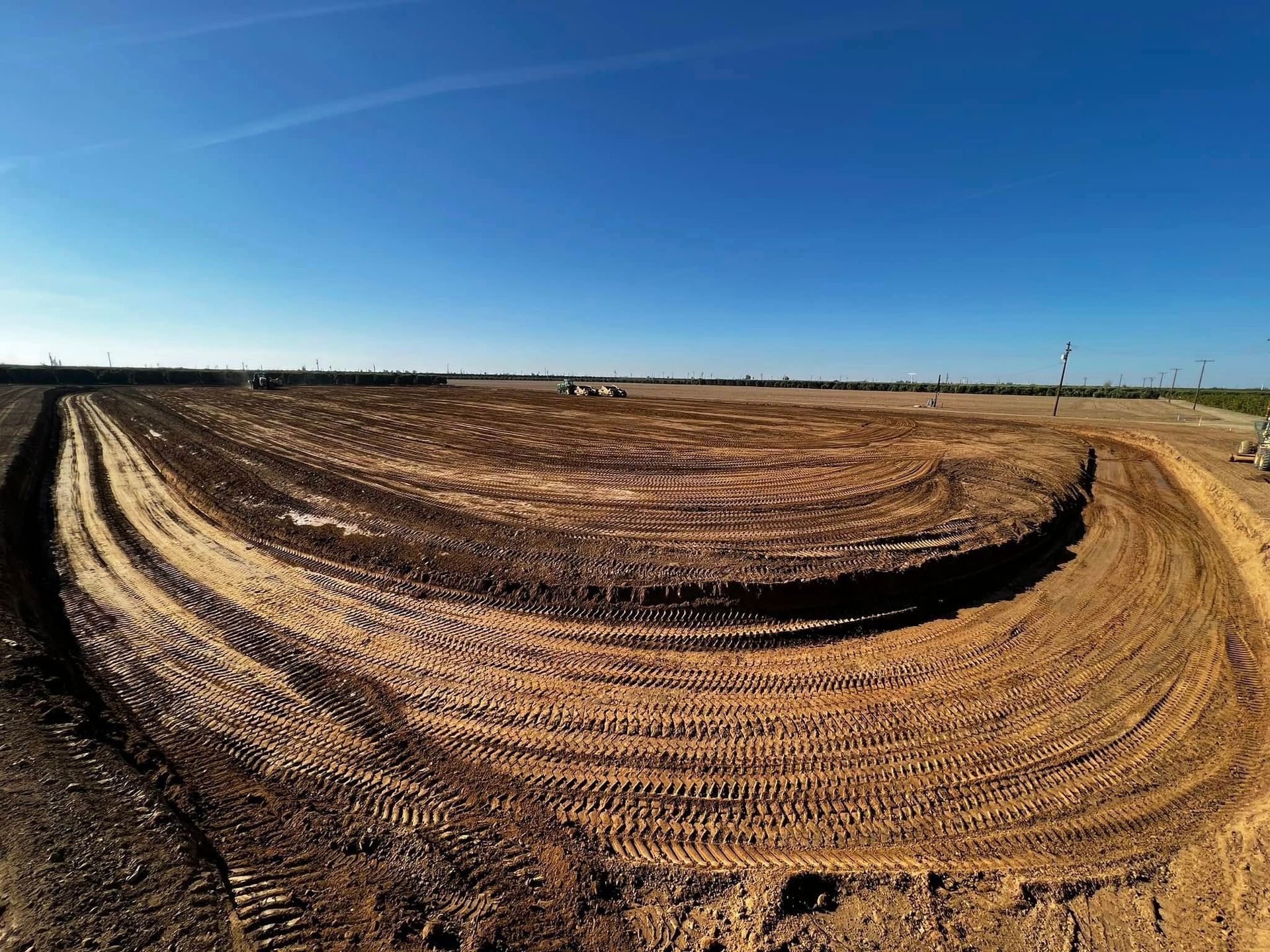 Curved dirt track in a brown, plowed field under a clear blue sky