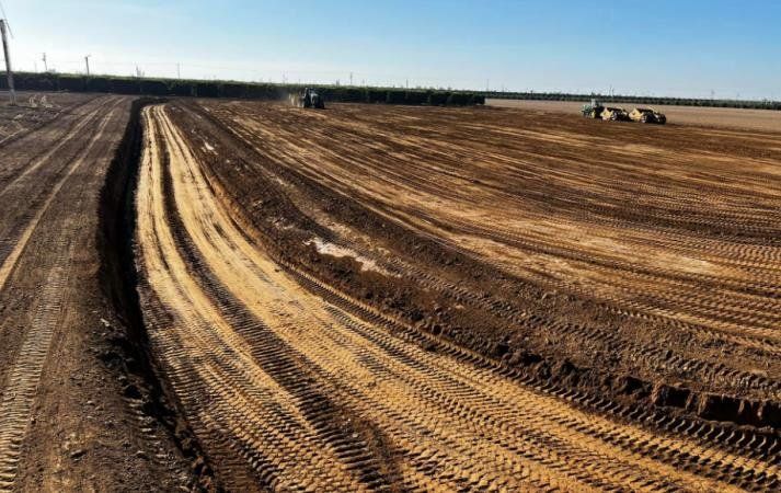 Wide farm field with freshly plowed soil and tractor tire tracks under a clear sky