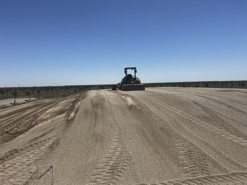 Bulldozer grading a wide dirt road under a clear blue sky in a flat, open landscape
