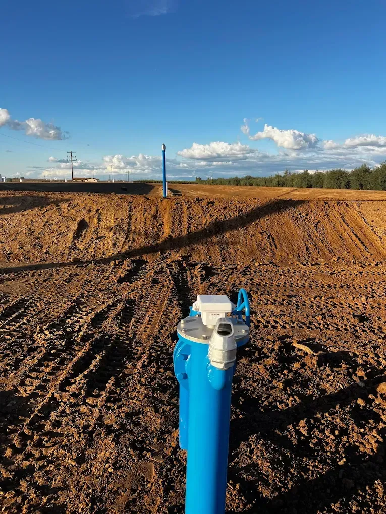 Blue irrigation pipe in a plowed field under a clear sky with clouds