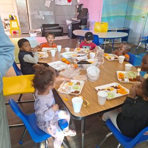 A group of children are sitting around a table with plates of food