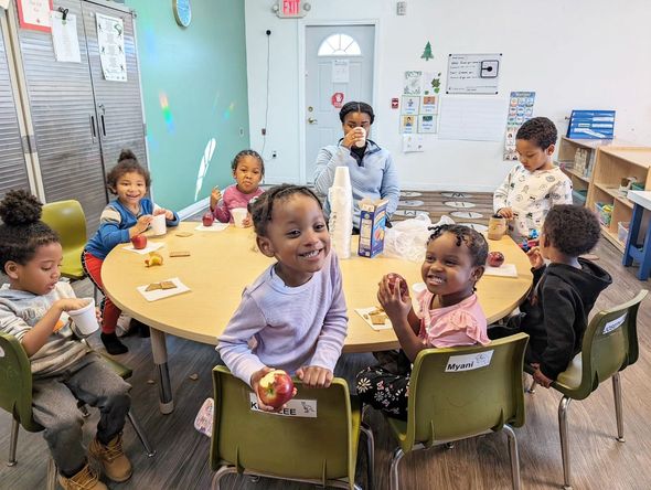 A group of children are sitting around a table in a classroom eating apples.