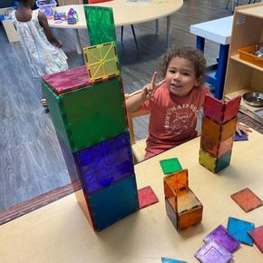 A little girl is sitting at a table playing with magnetic blocks.