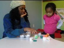 A woman and a little girl are sitting at a table playing with toys.