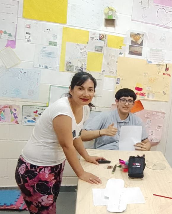Mujer y tres niños jugando con plastilina en una mesa; decoraciones coloridas.