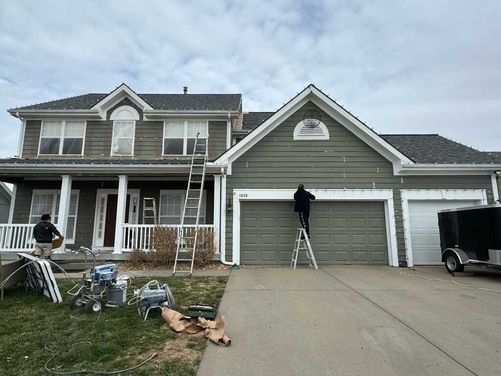 A Man Is Standing On A Ladder Painting The Front Of A House – Olathe, KS - JJR Painting