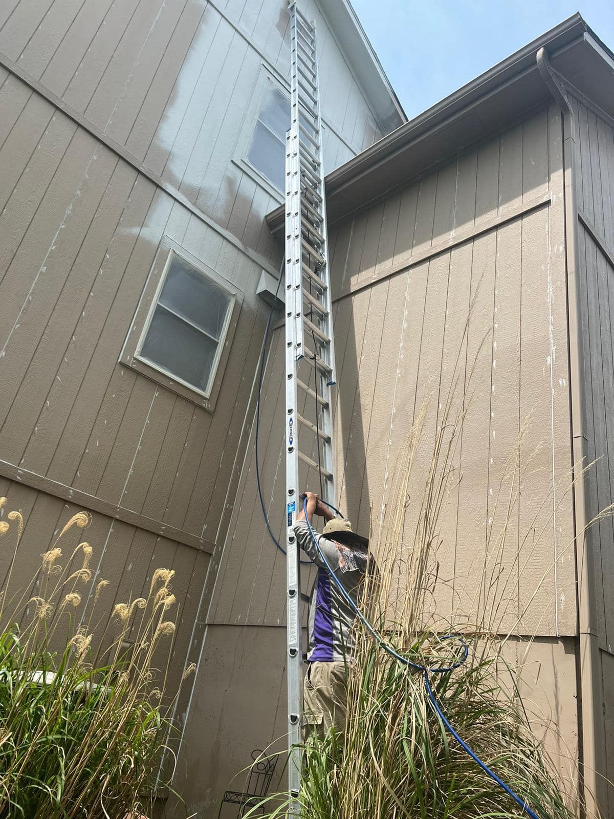A Man Is Standing On A Ladder Washing The Side Of A House – Olathe, KS - JJR Painting