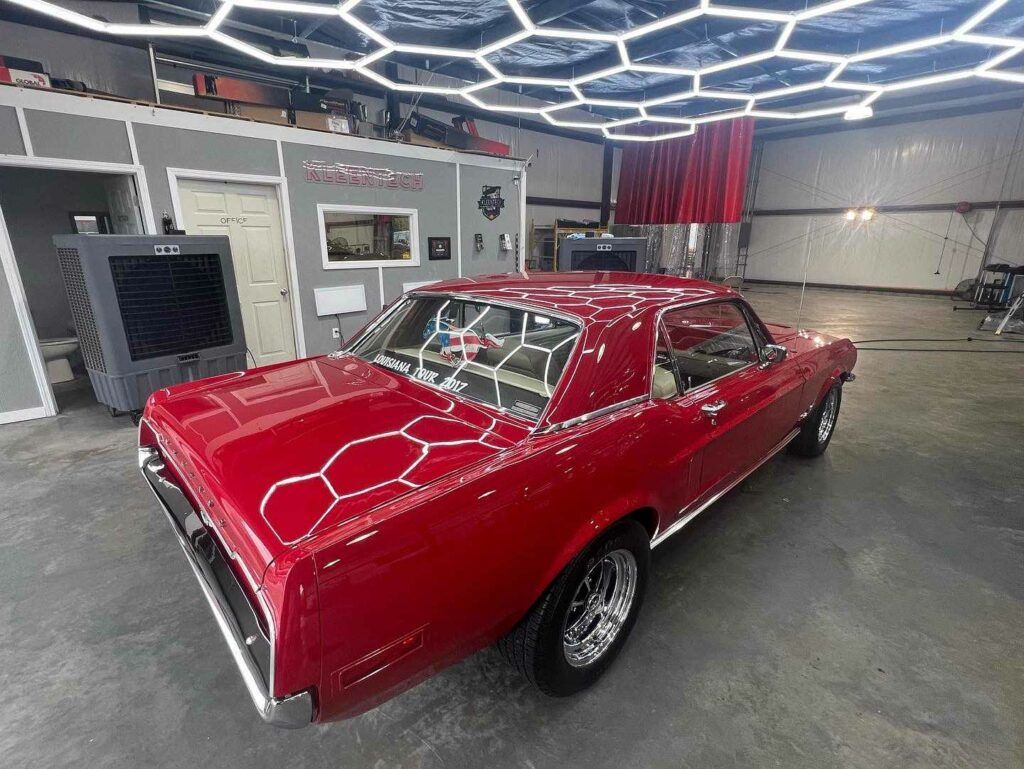 A red car is parked in a garage under a honeycomb ceiling.