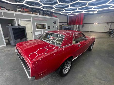 A red car is parked in a garage under a honeycomb ceiling.